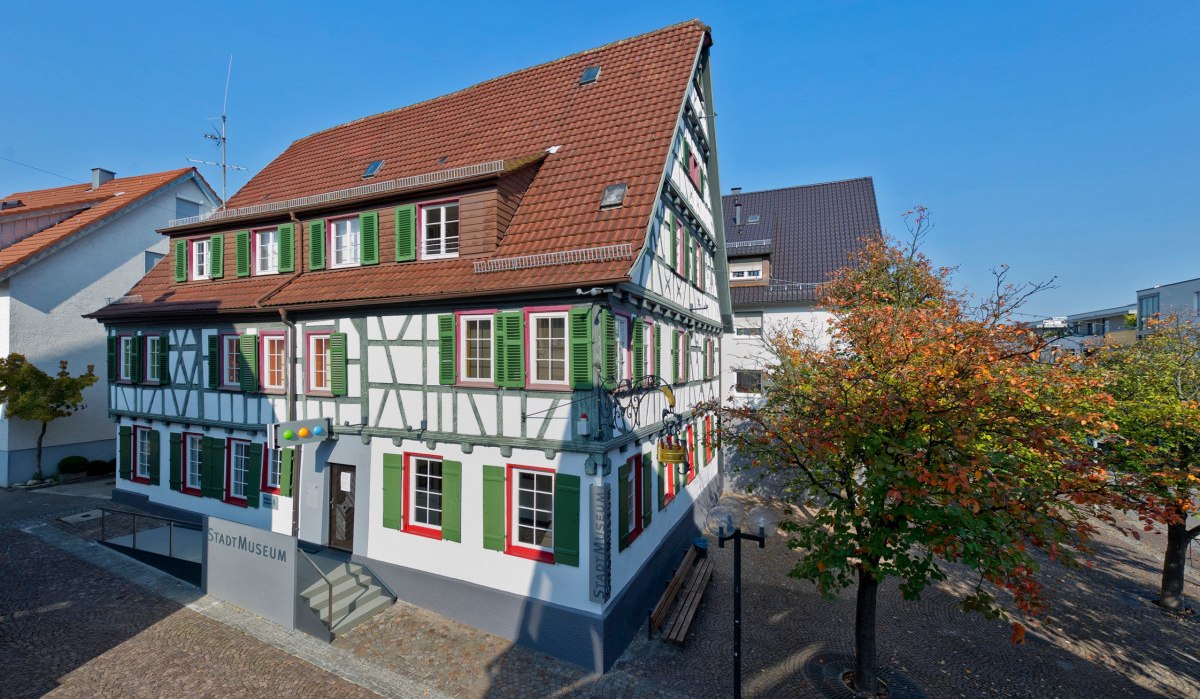 Fachwerkhaus mit grün-weißen Fensterläden, das Stadtmuseum Fellbach. Umgeben von Bäumen mit Herbstlaub und einem gepflasterten Platz., © Fellbach Tourismus Fachwerkhaus mit grün-weißen Fensterläden, das Stadtmuseum Fellbach. Umgeben von Bäumen mit Herbstlaub und einem gepflasterten Platz., © Fellbach Tourismus