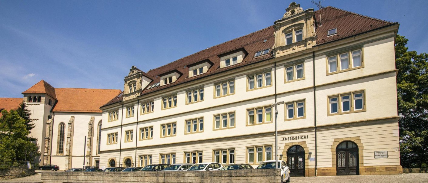 Ein historisches Gebäude mit rotem Ziegeldach und vielen Fenstern, beschriftet als Amtsgericht. Links ist ein weiteres Gebäude mit hohen Fenstern zu sehen., © Stuttgart-Marketing GmbH, Sarah Schmid