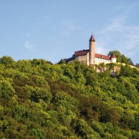 Burg Teck thront majestätisch auf einem bewaldeten Hügel, umgeben von dichtem Grün und unter einem klaren blauen Himmel., © SMG Achim Mende Burg Teck thront majestätisch auf einem bewaldeten Hügel, umgeben von dichtem Grün und unter einem klaren blauen Himmel., © SMG Achim Mende