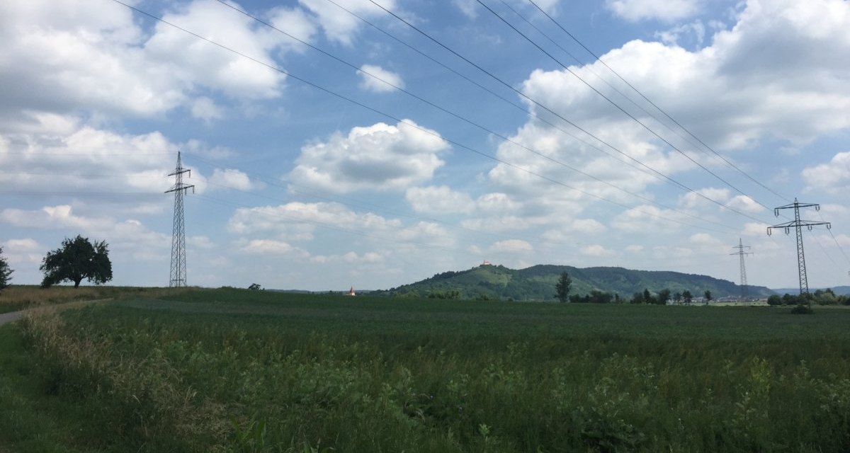 Weite Landschaft mit Stromleitungen und einem H&uuml;gel im Hintergrund, auf dem die Wurmlinger Kapelle steht. Der Himmel ist bew&ouml;lkt., &copy; www.pro-cycl.de