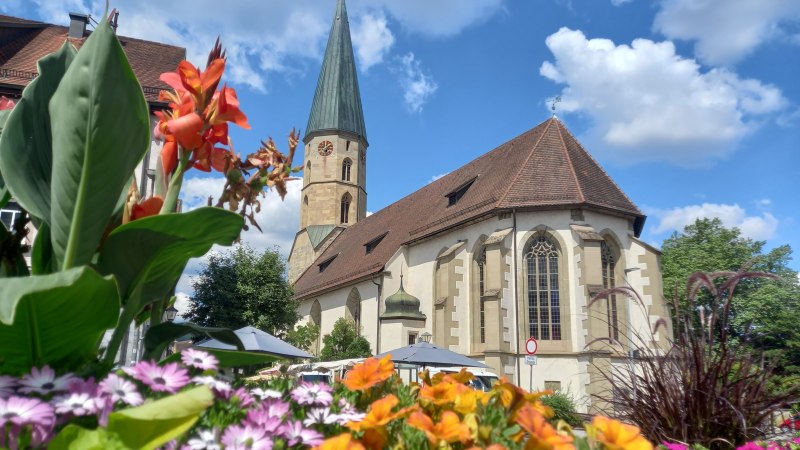 Kirche mit Kirchturm vor blauem Himmel mit weißen Wolken, davor bunte Sommerblumen, © Petra Natzkowski