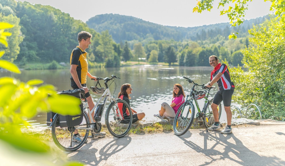 Vier Personen mit Fahrr&auml;dern genie&szlig;en die Natur an einem Seeufer. Zwei sitzen, zwei stehen mit Fahrr&auml;dern. Im Hintergrund bewaldete H&uuml;gel., &copy; Landratsamt G&ouml;ppingen