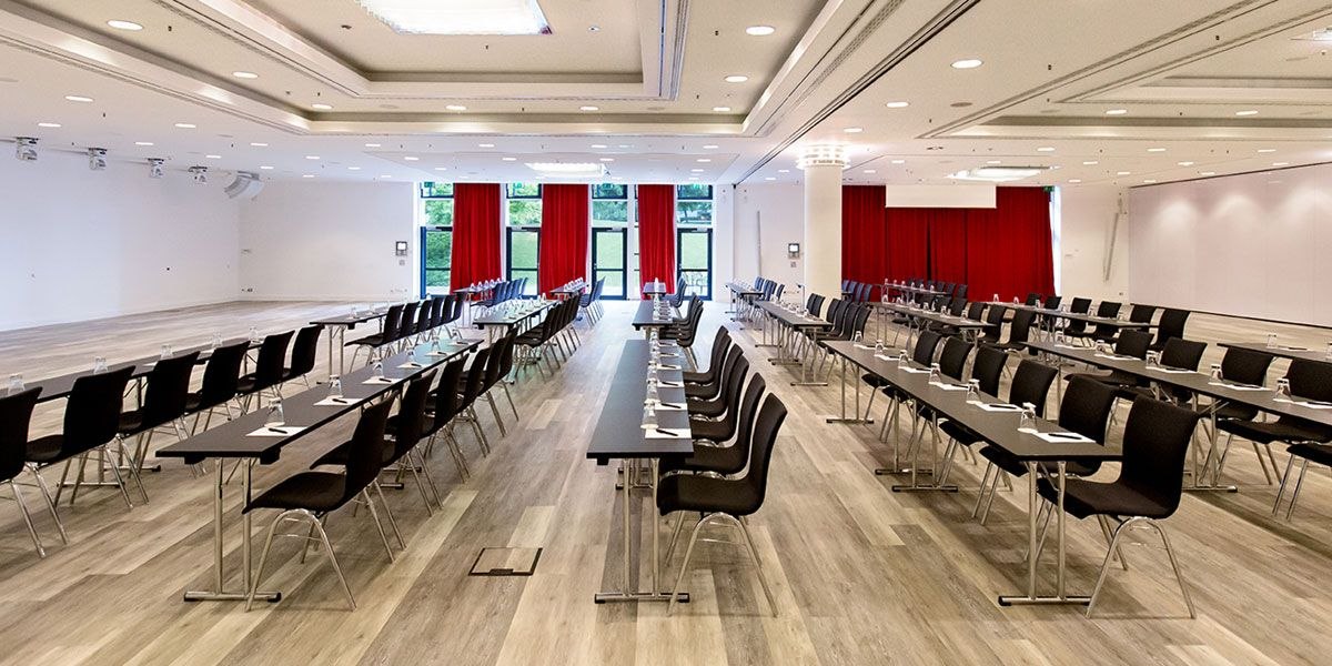 Großer Tagungsraum mit langen Tischen, schwarzen Stühlen, roten Vorhängen und heller Beleuchtung., © Dormero Hotel Stuttgart Großer Tagungsraum mit langen Tischen, schwarzen Stühlen, roten Vorhängen und heller Beleuchtung., © Dormero Hotel Stuttgart