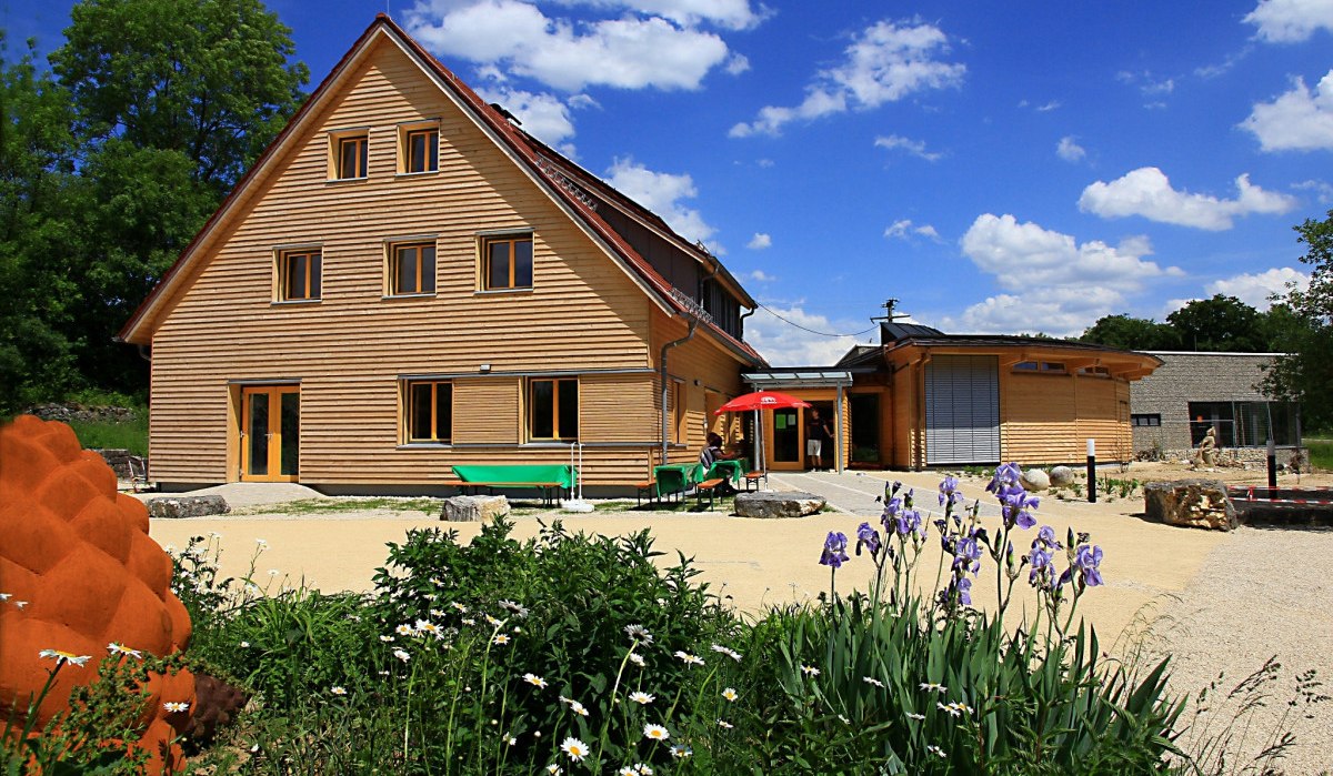 Modernes Holzgebäude mit Garten und Blumen im Vordergrund, blauer Himmel mit Wolken., © Naturschutzzentrum Schopflocher Alb Modernes Holzgebäude mit Garten und Blumen im Vordergrund, blauer Himmel mit Wolken., © Naturschutzzentrum Schopflocher Alb