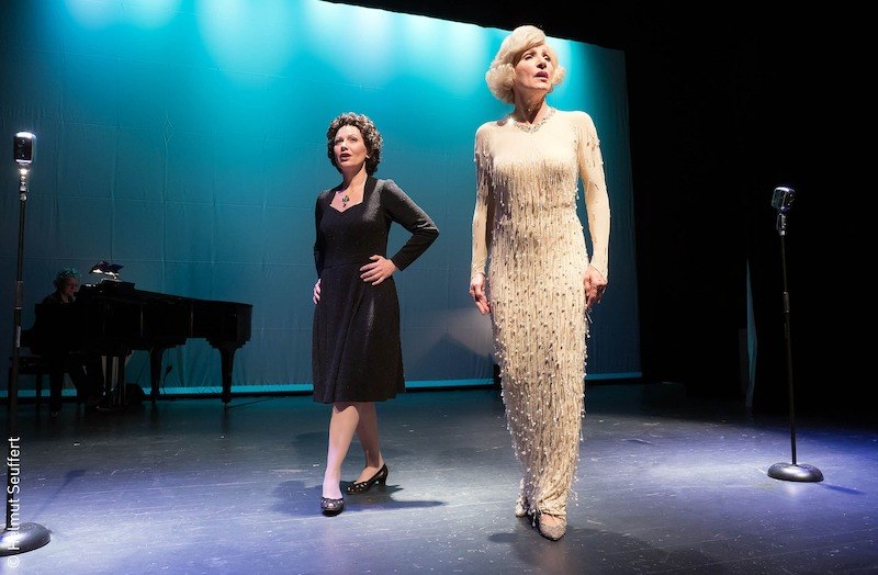 Zwei Frauen stehen auf einer Bühne, eine trägt ein schwarzes Kleid, die andere ein weißes. Im Hintergrund sind Mikrofone und ein Klavier zu sehen., © Stadt Kornwestheim Kulturmanagement