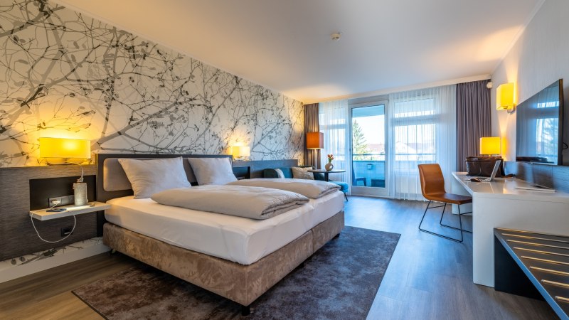 Modernes Hotelzimmer mit Doppelbett, Schreibtisch, Stuhl und Balkon. Helle Farben und stilvolle Wandgestaltung mit Naturmotiv., &copy; MASEVEN Stuttgart SI-Centrum