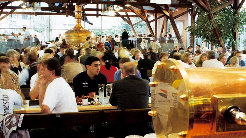 Ein belebtes Brauhaus mit vielen Menschen, die an Tischen sitzen. Im Hintergrund sind große Kupferkessel zu sehen., © Stuttgart-Marketing GmbH Ein belebtes Brauhaus mit vielen Menschen, die an Tischen sitzen. Im Hintergrund sind große Kupferkessel zu sehen., © Stuttgart-Marketing GmbH