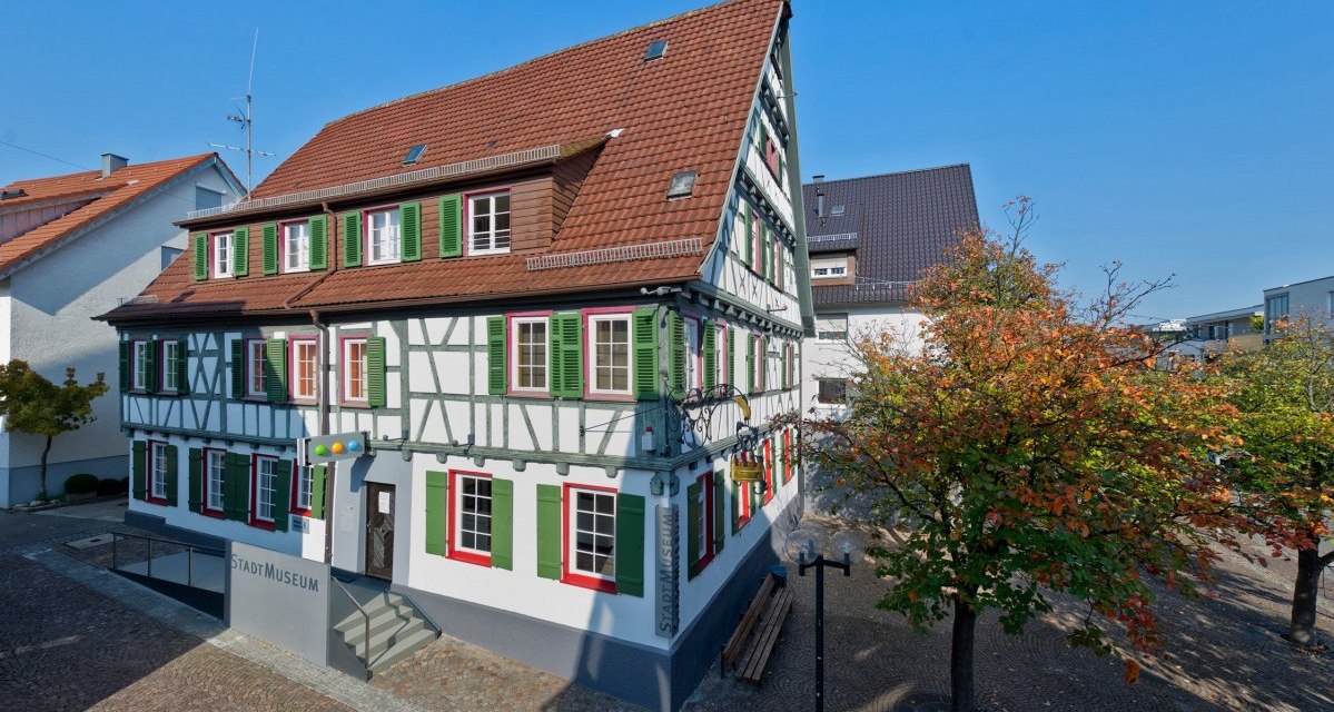 Fachwerkhaus mit grün-weißen Fensterläden, das Stadtmuseum Fellbach. Umgeben von Bäumen mit Herbstlaub und einem gepflasterten Platz., © Fellbach Tourismus Fachwerkhaus mit grün-weißen Fensterläden, das Stadtmuseum Fellbach. Umgeben von Bäumen mit Herbstlaub und einem gepflasterten Platz., © Fellbach Tourismus