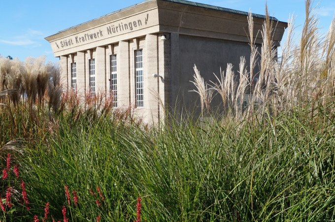Das alte Kraftwerk N&uuml;rtingen steht majest&auml;tisch hinter hohen Gr&auml;sern und bl&uuml;henden Pflanzen, ein Zeugnis industrieller Architektur., &copy; Stadt N&uuml;rtingen
