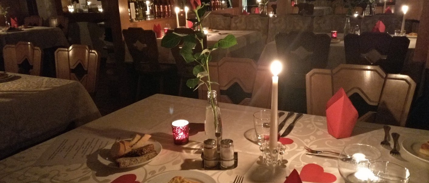 Ein romantisch gedeckter Tisch in einem Restaurant mit Kerzenlicht, Herzdekoration und Brot auf einem Teller. Im Hintergrund sind weitere Tische zu sehen., &copy; WeingutKr&auml;uterb&uuml;hl