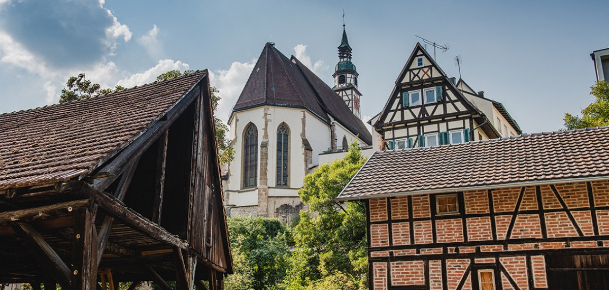 Fachwerkhäuser und eine Kirche mit Turm in Waiblingen, umgeben von Bäumen und blauem Himmel., © Unbekannt
