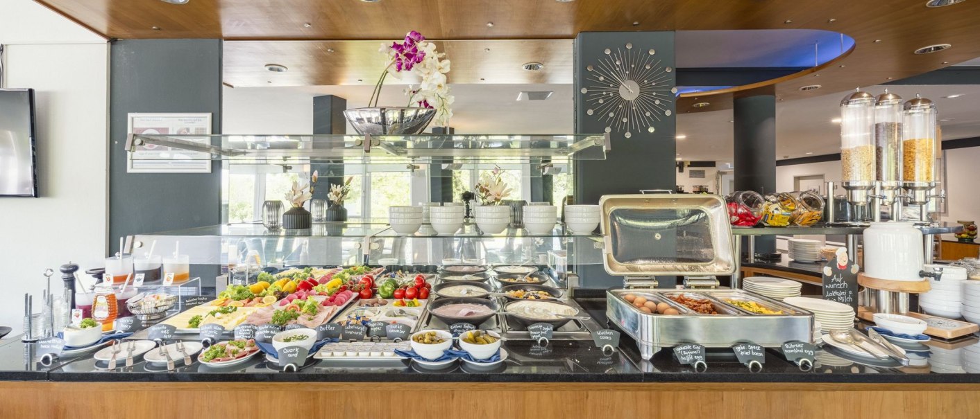 Ein Frühstücksbuffet mit einer Auswahl an Speisen wie Obst, Aufschnitt, Eiern und Müsli in einem modernen Restaurant., © Plaza INN Stuttgart-Filderstadt Ein Frühstücksbuffet mit einer Auswahl an Speisen wie Obst, Aufschnitt, Eiern und Müsli in einem modernen Restaurant., © Plaza INN Stuttgart-Filderstadt
