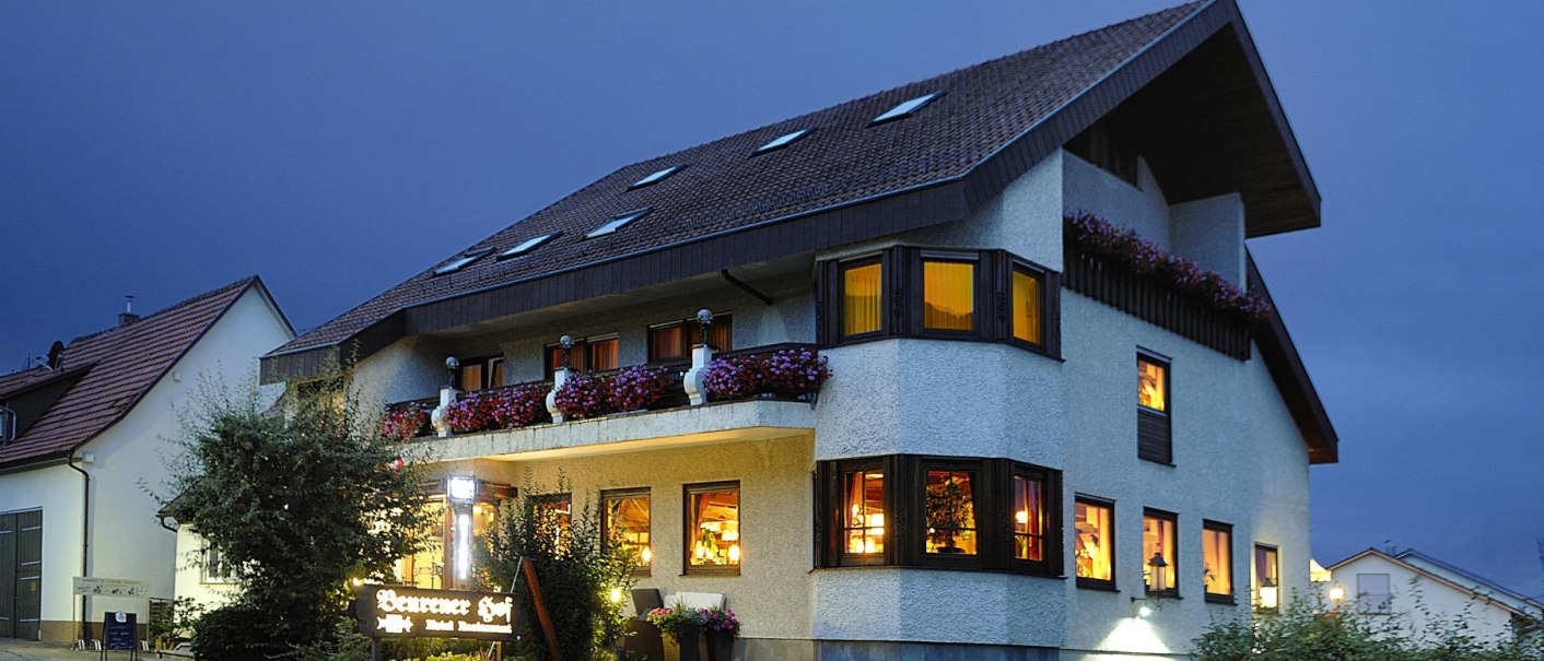 Beleuchtetes Gebäude bei Nacht mit Blumen auf dem Balkon und einem Schild "Beurener Hof". Der Himmel ist dunkelblau., © Hotel & Restaurant Beurener Hof Beleuchtetes Gebäude bei Nacht mit Blumen auf dem Balkon und einem Schild "Beurener Hof". Der Himmel ist dunkelblau., © Hotel & Restaurant Beurener Hof