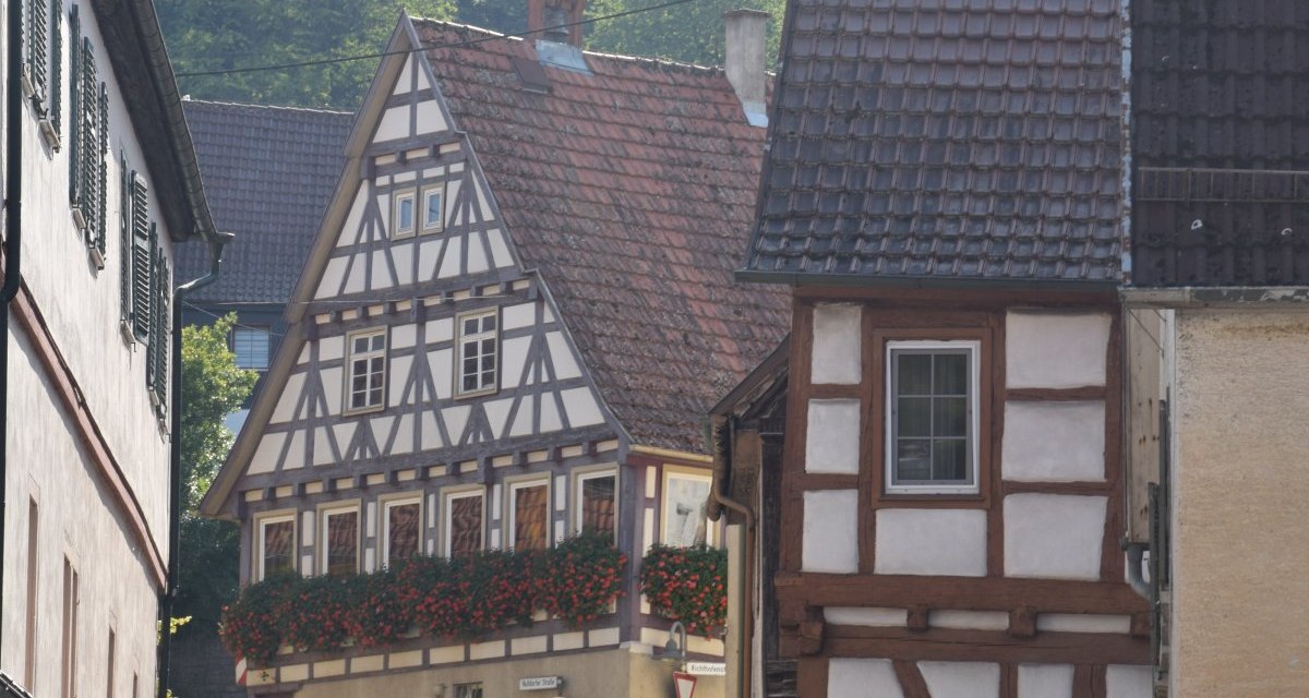 Fachwerkh&auml;user in einer engen, kurvigen Stra&szlig;e mit Blumen an den Fenstern und einem H&uuml;gel im Hintergrund., &copy; Land der 1000 H&uuml;gel - Kraichgau-Stromberg