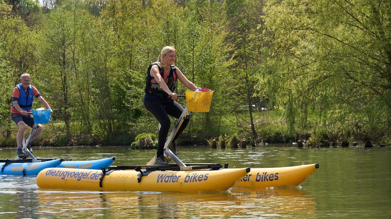 Zwei Personen fahren auf gelben Wasserfahrrädern auf einem Fluss. Sie tragen Schwimmwesten und sind von grüner Natur umgeben., © Foto LKZ - Fotograf Andreas Becker Zwei Personen fahren auf gelben Wasserfahrrädern auf einem Fluss. Sie tragen Schwimmwesten und sind von grüner Natur umgeben., © Foto LKZ - Fotograf Andreas Becker