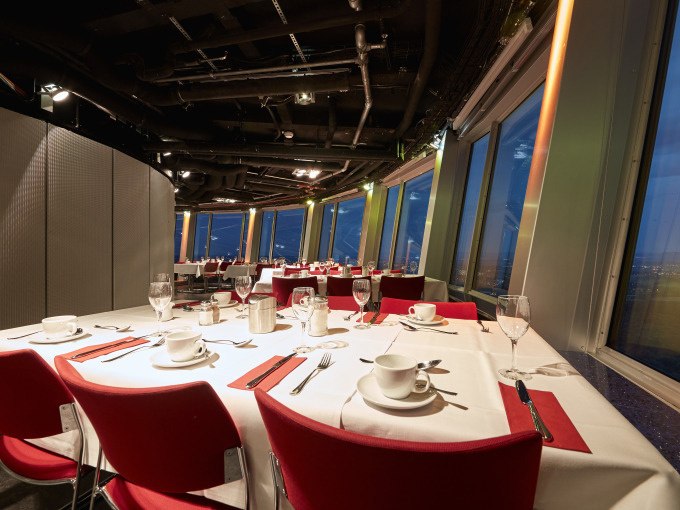 Elegantes Café mit gedeckten Tischen, rotem Dekor und Panoramafenstern, die einen nächtlichen Stadtblick bieten., © SWR Media Services GmbH / SWR Fernsehturm Stuttgart