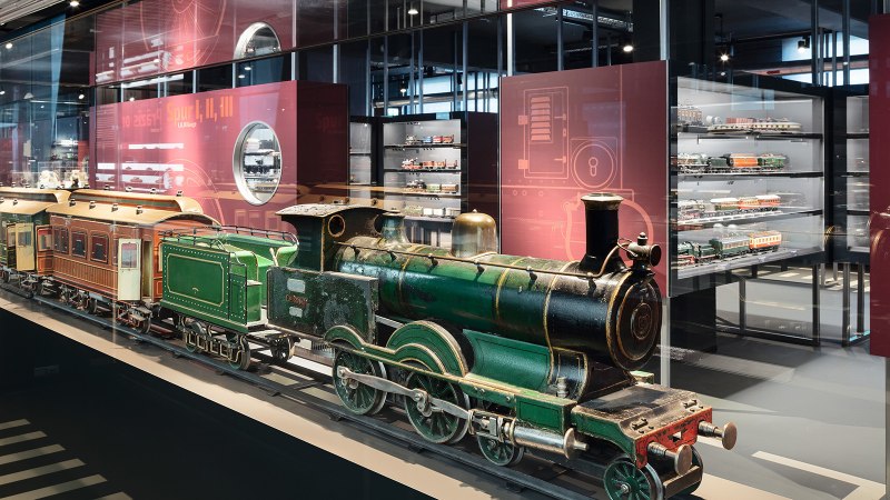 Eine grüne Modelllokomotive in einer Glasvitrine, umgeben von weiteren Modelleisenbahnen in einem Museumsausstellungsraum., © Märklineum Eine grüne Modelllokomotive in einer Glasvitrine, umgeben von weiteren Modelleisenbahnen in einem Museumsausstellungsraum., © Märklineum