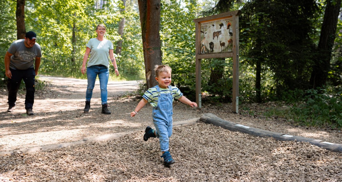 Ein Kind rennt lachend auf einem Waldweg, während zwei Erwachsene ihm folgen. Im Hintergrund steht ein Informationsschild., © Stadtmarketing Weil der Stadt Ein Kind rennt lachend auf einem Waldweg, während zwei Erwachsene ihm folgen. Im Hintergrund steht ein Informationsschild., © Stadtmarketing Weil der Stadt