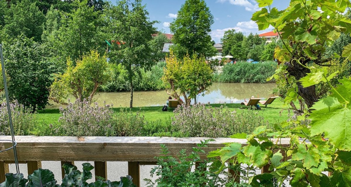 Ein gr&uuml;ner Garten mit Pflanzen im Vordergrund, ein Fluss und Liegest&uuml;hle im Hintergrund unter blauem Himmel., &copy; Remstal Tourismus e.V.