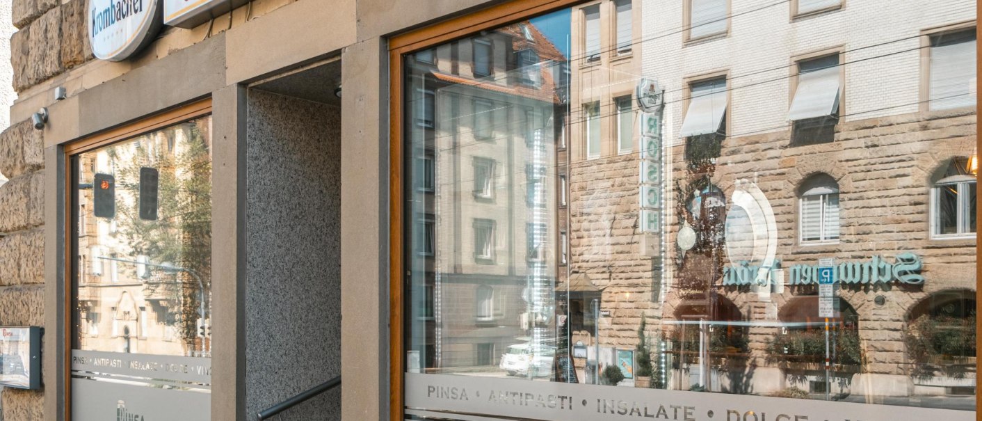 Außenansicht eines Restaurants mit der Aufschrift 'Pinsa Manufaktur' und Spiegelung von Gebäuden im Fenster., © SMG, Sarah Schmid
