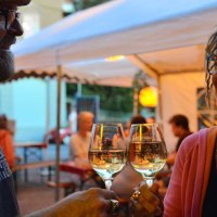 Zwei Personen stoßen lächelnd mit Weingläsern an, unter einem Zelt bei einem sommerlichen Event., © Weingut Ruoff