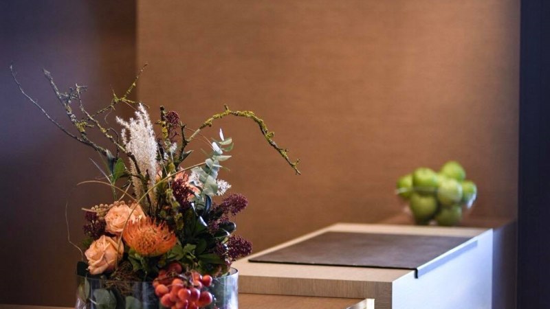 Elegante Rezeption mit Blumenarrangement und modernen H&auml;ngelampen. Im Hintergrund eine Schale mit gr&uuml;nen &Auml;pfeln., &copy; TOMAS