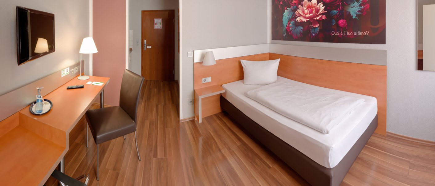 Modernes Einzelzimmer mit Holzboden, Einzelbett, Schreibtisch, Stuhl und großem Blumenbild an der Wand., © attimo Hotel Stuttgart