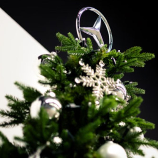Ein Weihnachtsbaum mit einem Mercedes-Stern als Spitze, geschmückt mit silbernen Kugeln und Schneeflocken vor dunklem Hintergrund., © Mercedes-Benz AG Ein Weihnachtsbaum mit einem Mercedes-Stern als Spitze, geschmückt mit silbernen Kugeln und Schneeflocken vor dunklem Hintergrund., © Mercedes-Benz AG
