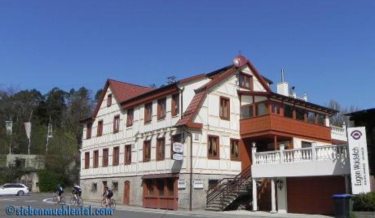 Ein traditionelles Fachwerkgebäude mit rotem Dach und Balkon. Drei Radfahrer fahren vorbei. Der Himmel ist klar und blau., © Natur.Nah. Schönbuch & Heckengäu Ein traditionelles Fachwerkgebäude mit rotem Dach und Balkon. Drei Radfahrer fahren vorbei. Der Himmel ist klar und blau., © Natur.Nah. Schönbuch & Heckengäu