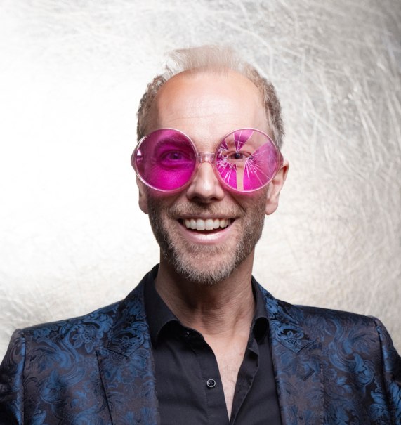 Ein Mann mit rosa Brille und blauem Jackett lächelt vor einem hellen Hintergrund., © Stadt Leinfelden-Echterdingen, Kulturamt