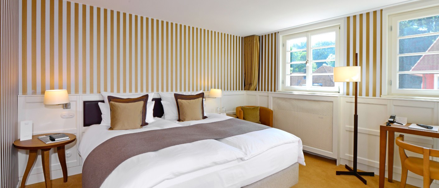 Klassisches Hotelzimmer mit gestreifter Tapete, Doppelbett, Schreibtisch und Stehlampe. Große Fenster lassen viel Licht herein., © Waldhotel Stuttgart GmbH Klassisches Hotelzimmer mit gestreifter Tapete, Doppelbett, Schreibtisch und Stehlampe. Große Fenster lassen viel Licht herein., © Waldhotel Stuttgart GmbH