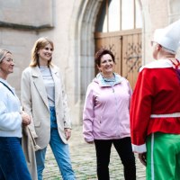 Drei Frauen unterhalten sich mit einer Person in einem bunten Kost&uuml;m vor einem historischen Geb&auml;ude. Die Szene wirkt fr&ouml;hlich und entspannt., &copy; Stadt N&uuml;rtingen
