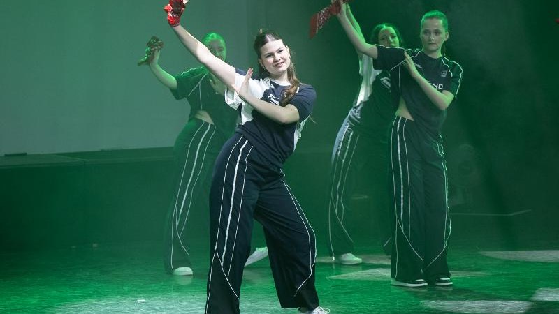 Kinder tanzen Hip-Hop auf einer Bühne, tragen schwarze Outfits und rote Tücher. Die Beleuchtung ist grün und die Stimmung dynamisch., © Kunstschule Labyrinth