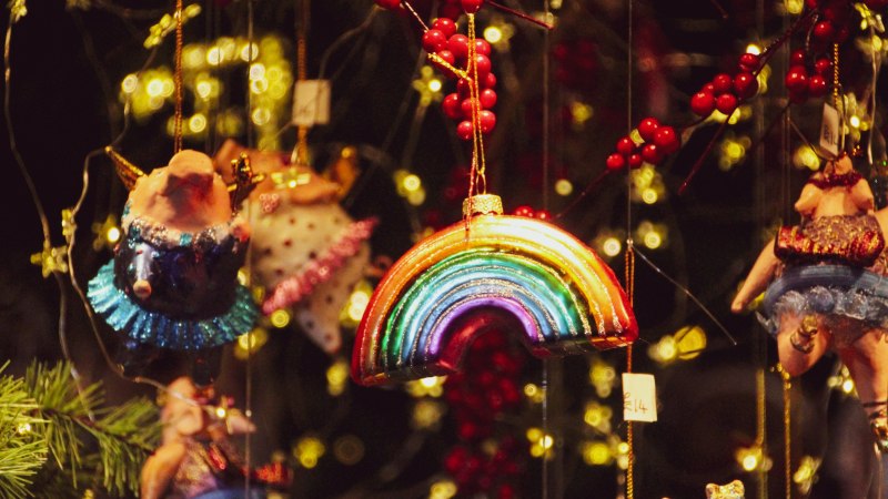 Bunter Weihnachtsschmuck mit Regenbogen und Schweinchen, umgeben von roten Beeren und Lichtern auf einem Weihnachtsmarkt., © Stadt Metzingen Bunter Weihnachtsschmuck mit Regenbogen und Schweinchen, umgeben von roten Beeren und Lichtern auf einem Weihnachtsmarkt., © Stadt Metzingen