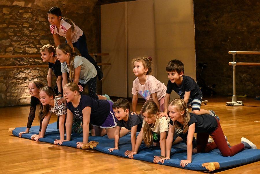 Kinder bauen eine menschliche Pyramide auf einer blauen Matte in einem Raum mit Steinwand und Holzboden., © Kunstschule Labyrinth Kinder bauen eine menschliche Pyramide auf einer blauen Matte in einem Raum mit Steinwand und Holzboden., © Kunstschule Labyrinth