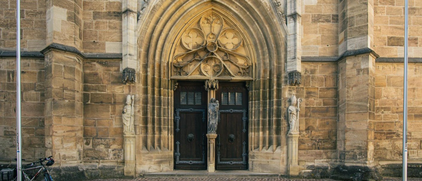 Eingang des Heilig-Kreuz-Münsters in Schwäbisch Gmünd mit kunstvoll verzierten Türen und steinernen Figuren. Ein Fahrrad steht links neben dem Eingang., © Stuttgart-Marketing GmbH, Sarah Schmid Eingang des Heilig-Kreuz-Münsters in Schwäbisch Gmünd mit kunstvoll verzierten Türen und steinernen Figuren. Ein Fahrrad steht links neben dem Eingang., © Stuttgart-Marketing GmbH, Sarah Schmid