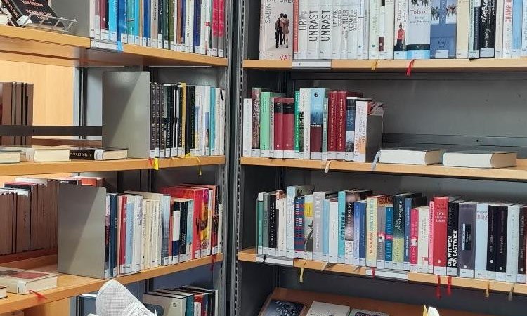 Eine Person liegt entspannt auf einem roten Sitzsack in einer Bibliothek und liest ein gelbes Buch. Umgeben von B&uuml;cherregalen voller B&uuml;cher., &copy; (c) Regina Gobert