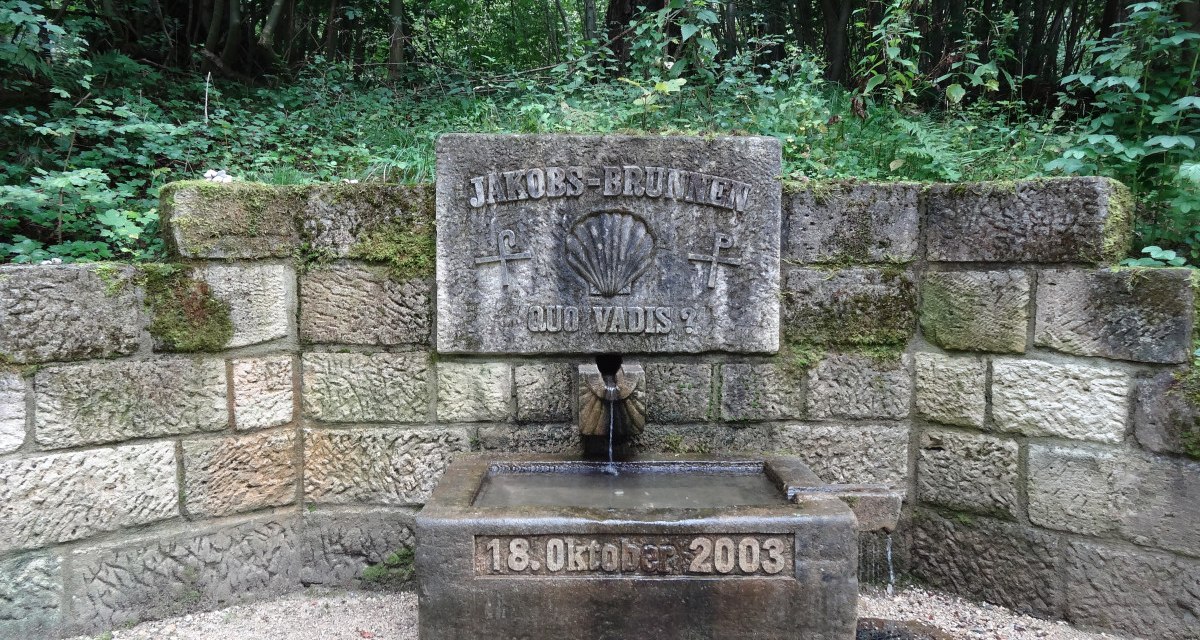 Steinerner Jakobsbrunnen im Wald, mit Inschrift 'Quo Vadis?' und Datum 18. Oktober 2003. Umgeben von grüner Vegetation., © Nürtingen - Stuttgart-Marketing GmbH