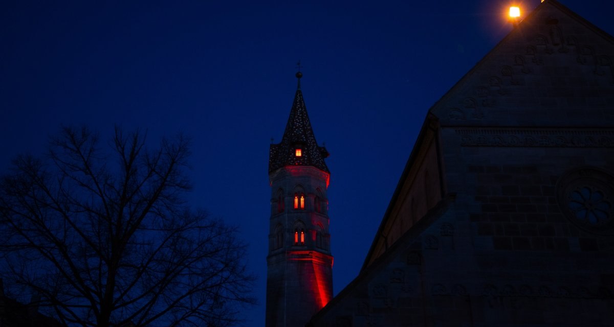 Es ist Nacht, der Himmel ist dunkelblau, der Johannisturm wird mit rotem Licht beleuchtet. Neben dem Turm steht ein Baum., © Foto: Mario Klaiber Es ist Nacht, der Himmel ist dunkelblau, der Johannisturm wird mit rotem Licht beleuchtet. Neben dem Turm steht ein Baum., © Foto: Mario Klaiber