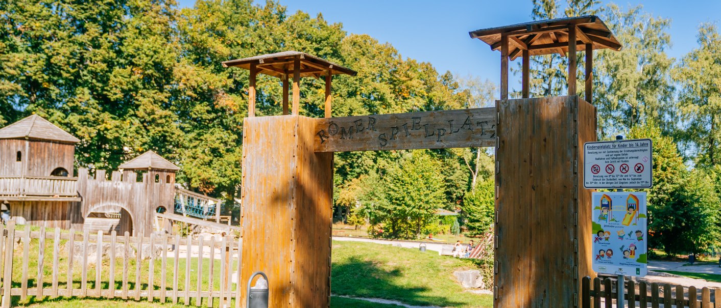 Eingang zum R&ouml;mer-Spielplatz mit Holztor und Schildern. Im Hintergrund sind B&auml;ume und ein h&ouml;lzernes Spielger&uuml;st zu sehen., &copy; Stuttgart-Marketing GmbH, Thomas Niederm&uuml;ller