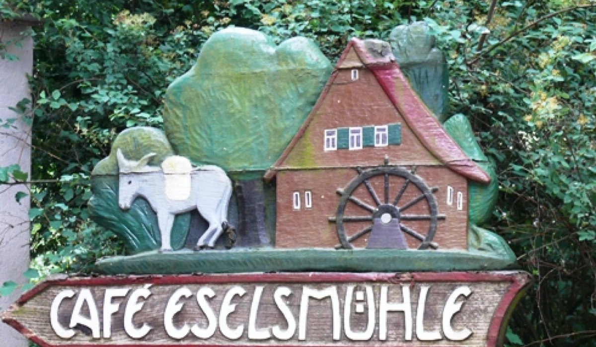 Holzschild mit einem Esel, einer Mühle und der Aufschrift 'Café Eselsmühle' vor grünem Hintergrund., © Natur.Nah. Schönbuch & Heckengäu Holzschild mit einem Esel, einer Mühle und der Aufschrift 'Café Eselsmühle' vor grünem Hintergrund., © Natur.Nah. Schönbuch & Heckengäu