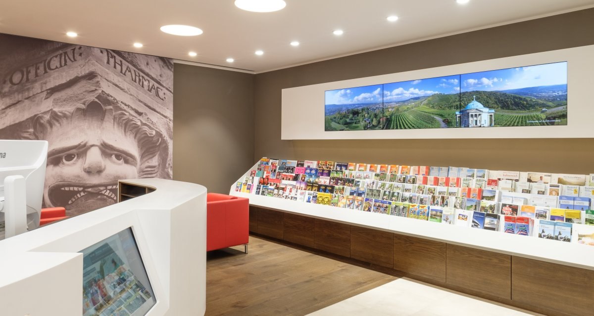 Moderne Touristinformation mit Prospektwand, Bildschirmen und einem Empfangstresen. Ein großes Wandbild zeigt ein antikes Gesicht., © Waiblingen - Stuttgart-Marketing GmbH Moderne Touristinformation mit Prospektwand, Bildschirmen und einem Empfangstresen. Ein großes Wandbild zeigt ein antikes Gesicht., © Waiblingen - Stuttgart-Marketing GmbH