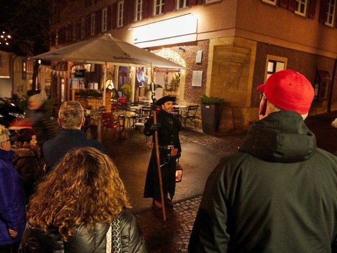 Ein Nachtwächter in historischer Kleidung führt eine Gruppe durch eine nächtliche, beleuchtete Straße., © Stadt Waldenbuch