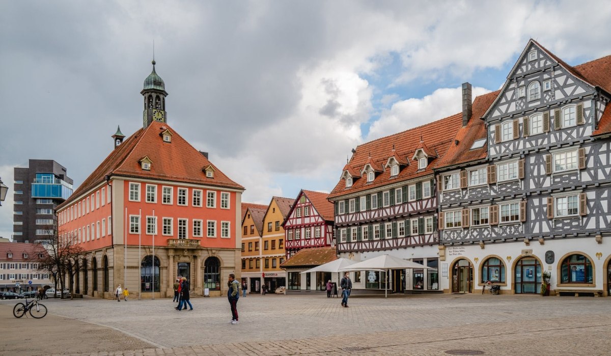 Der Marktplatz in Schorndorf zeigt historische Fachwerkh&auml;user und ein rotes Geb&auml;ude mit Turm. Menschen spazieren &uuml;ber den Platz.