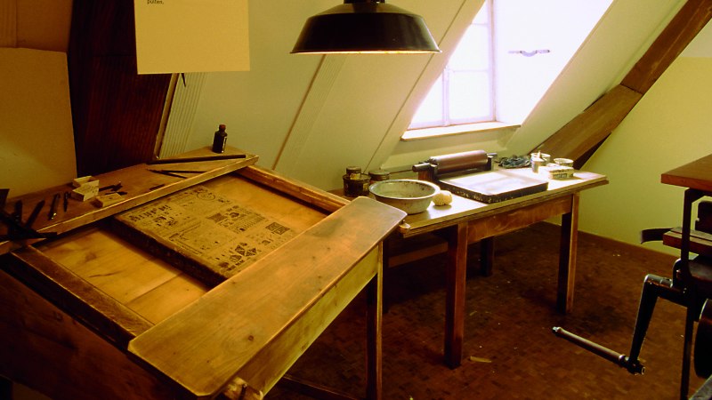 Historische Druckwerkstatt im J.-F.-Schreiber Museum Esslingen mit Holztischen, Druckutensilien und einem Fenster im Hintergrund., © Esslinger Stadtmarketing & Tourismus GmbH
