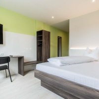 Modernes Einzelzimmer mit Bett, Schreibtisch, Stuhl und Fernseher. Die Wände sind in Grün und Weiß gehalten, das Mobiliar ist aus dunklem Holz., © a2 HOTELS am Quadrium