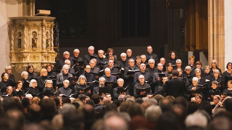 Ein Chor in schwarzer Kleidung singt in einer Kirche, dirigiert von einer Person. Die Kirche ist voll besetzt., © Ev. Bezirkskantorat Schorndorf Ein Chor in schwarzer Kleidung singt in einer Kirche, dirigiert von einer Person. Die Kirche ist voll besetzt., © Ev. Bezirkskantorat Schorndorf
