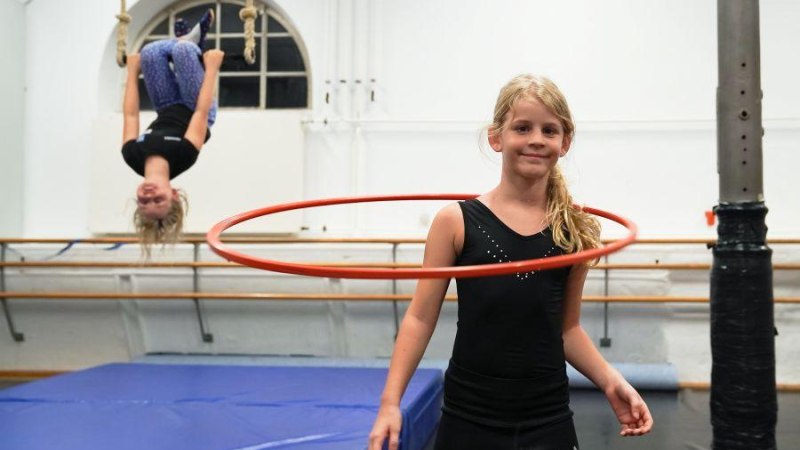 Ein Mädchen mit Hula-Hoop-Reifen lächelt, während ein anderes kopfüber an Seilen hängt. Zirkus-Workshop für Kinder in Ludwigsburg., © Kunstschule Labyrinth Ein Mädchen mit Hula-Hoop-Reifen lächelt, während ein anderes kopfüber an Seilen hängt. Zirkus-Workshop für Kinder in Ludwigsburg., © Kunstschule Labyrinth