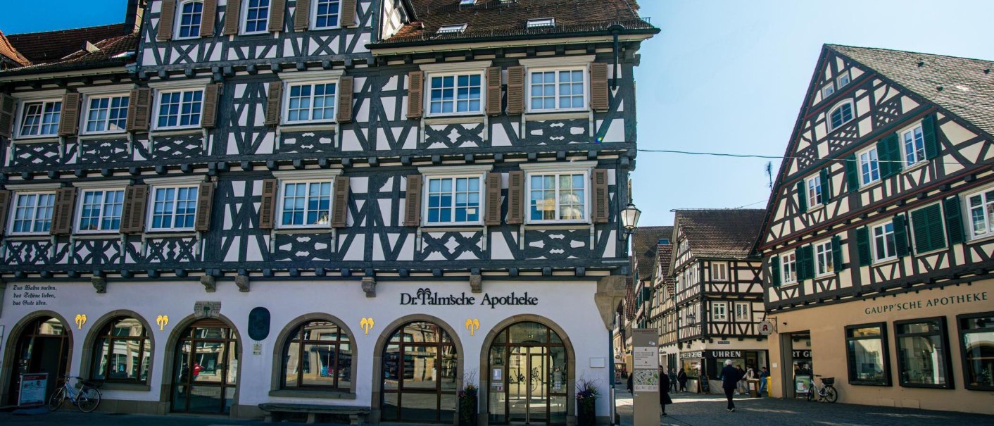 Fachwerkhäuser am Marktplatz in Schorndorf. Zwei Apotheken im Erdgeschoss, Passanten und Fahrräder. Sonniger Tag mit klarem Himmel., © Stuttgart-Marketing GmbH, Sarah Schmid Fachwerkhäuser am Marktplatz in Schorndorf. Zwei Apotheken im Erdgeschoss, Passanten und Fahrräder. Sonniger Tag mit klarem Himmel., © Stuttgart-Marketing GmbH, Sarah Schmid