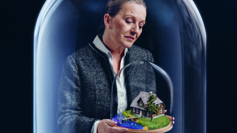 Eine Frau betrachtet ein Miniaturhaus unter einer Glaskuppel. Das Modell zeigt ein Haus mit Garten und kleinem Fluss., &copy; Manuel Wagner